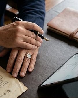 Mãos assinando um documento à mesa, ao lado de um tablet
